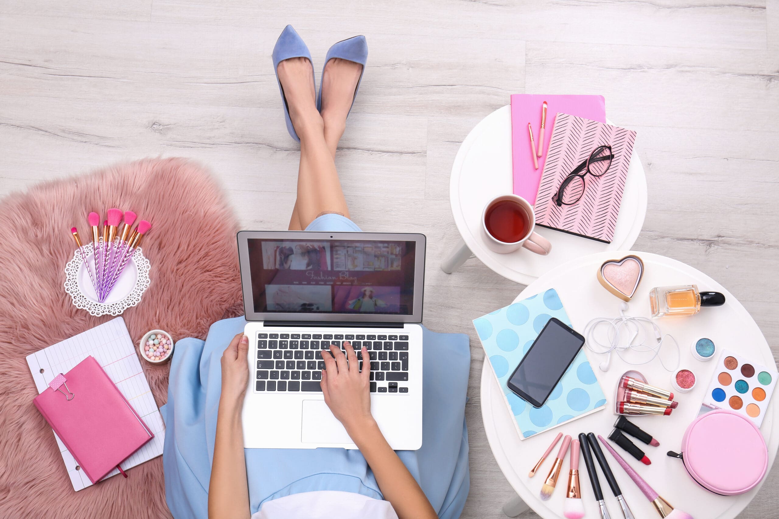 Beauty blogger with laptop and cosmetics sitting on floor, top view