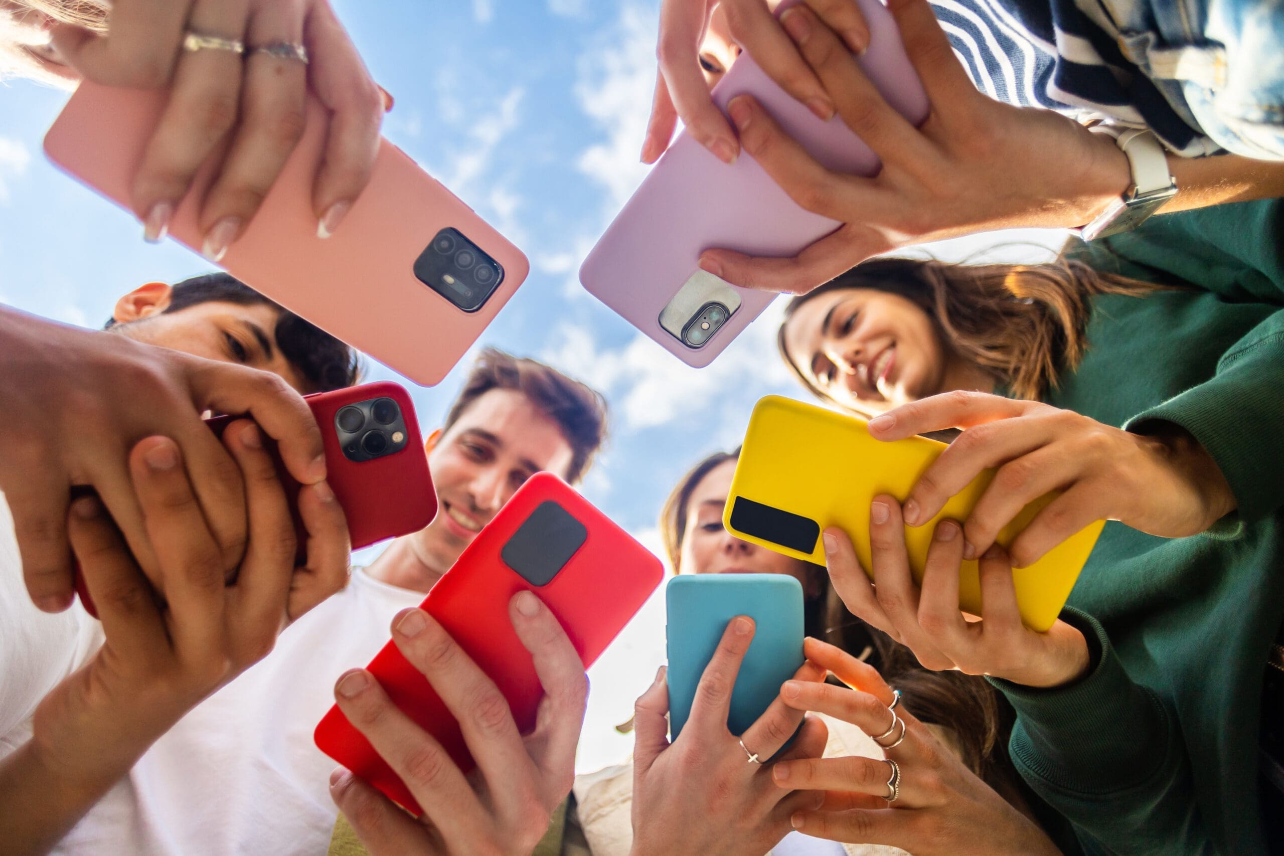 Young group of people using mobile phone device standing in circle outdoors